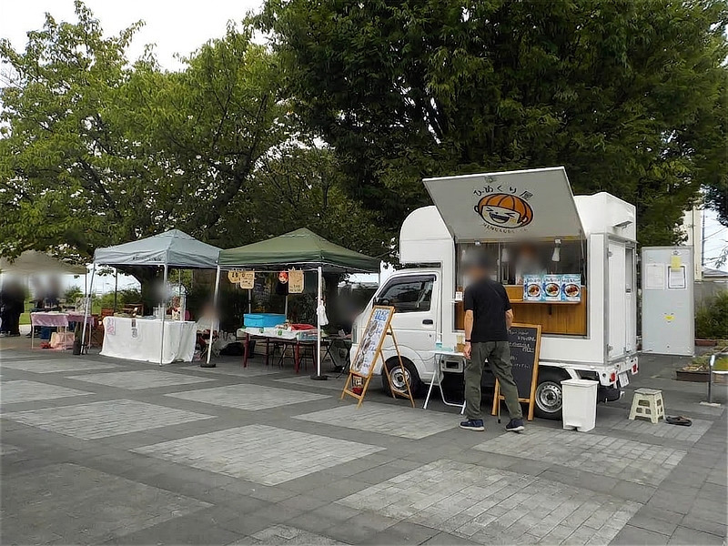 キッチンカー『ひめくり屋』の白い車両と、その横に並ぶ緑と灰色のマルシェテント。男性客がメニューを見ている様子。