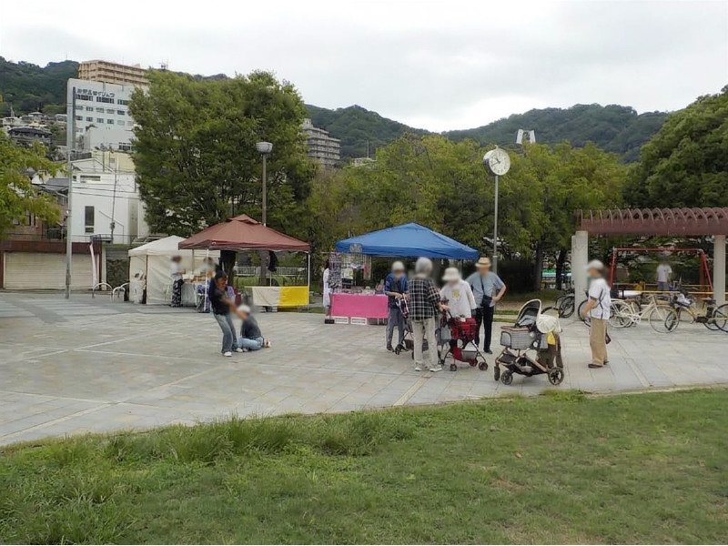 東石切公園の広場に立てられた青と茶色のテント。来場者や子供連れが集まり、静かな雰囲気の中でマルシェを楽しんでいる全景。