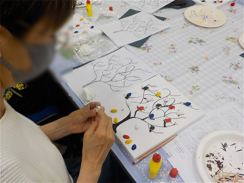 木の枝が描かれたパネルに、色とりどりの小鳥を配置していく手元の様子