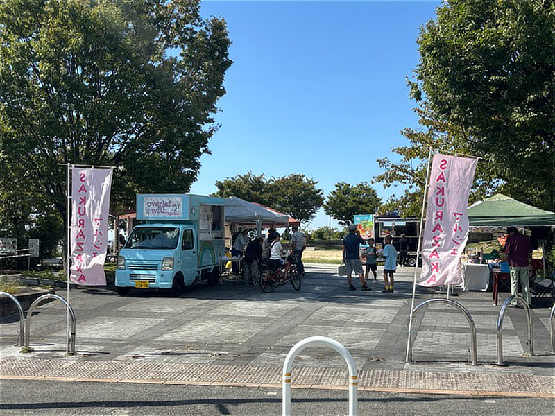 東石切公園で開催されたSAKURAZAKAマルシェの会場風景。青空の下、キッチンカーやテントが並ぶ。